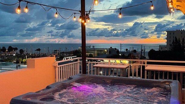 A hot tub on a balcony with string lights and a view of the ocean and buildings.