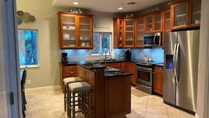 A modern kitchen with wooden cabinets, a stainless steel refrigerator, and a large island with bar stools.