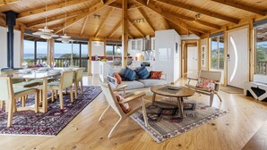 A spacious room with a high wooden ceiling, a dining area with a table and chairs, a sofa, and a small round table with a chair. - Peace & Plenty - beachfront hideaway with an indoor heated pool (Dolphin Sands)