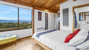 A bedroom with a large window, wooden ceiling, and a bed with pillows. - Peace & Plenty - beachfront hideaway with an indoor heated pool (Dolphin Sands)