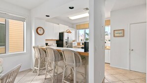 Een moderne keuken met witte kasten, een centraal eiland met barkrukken, een magnetron en een koelkast.