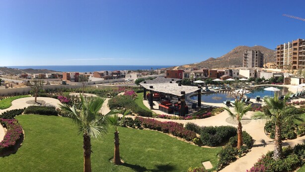 A resort with a pool, palm trees, and a view of the ocean. - New Condo Copala/Quivira Golf Club (Cabo San Lucas)