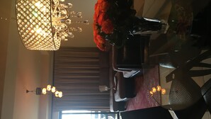 A dining area with a chandelier, a vase of red flowers, and a view of the outside through a window. - New Condo Copala/Quivira Golf Club (Cabo San Lucas)