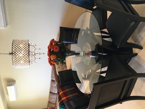 Un comedor con una mesa de vidrio, sillas negras, una araña y un florero con flores anaranjadas.