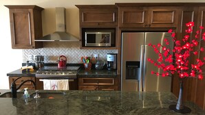 A kitchen with dark wooden cabinets, a stainless steel refrigerator, a microwave, and a coffee maker. - New Condo Copala/Quivira Golf Club (Cabo San Lucas)