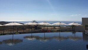A pool area with umbrellas, a clear sky, and a view of the sea. - New Condo Copala/Quivira Golf Club (Cabo San Lucas)