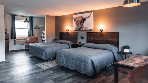A modern bedroom with two beds, a wooden headboard, a small table, and a hanging light fixture. - Newport Motel (Newport)