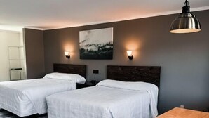 A hotel room with two beds, a wooden floor, a small table, and a painting on the wall. - Newport Motel (Newport)