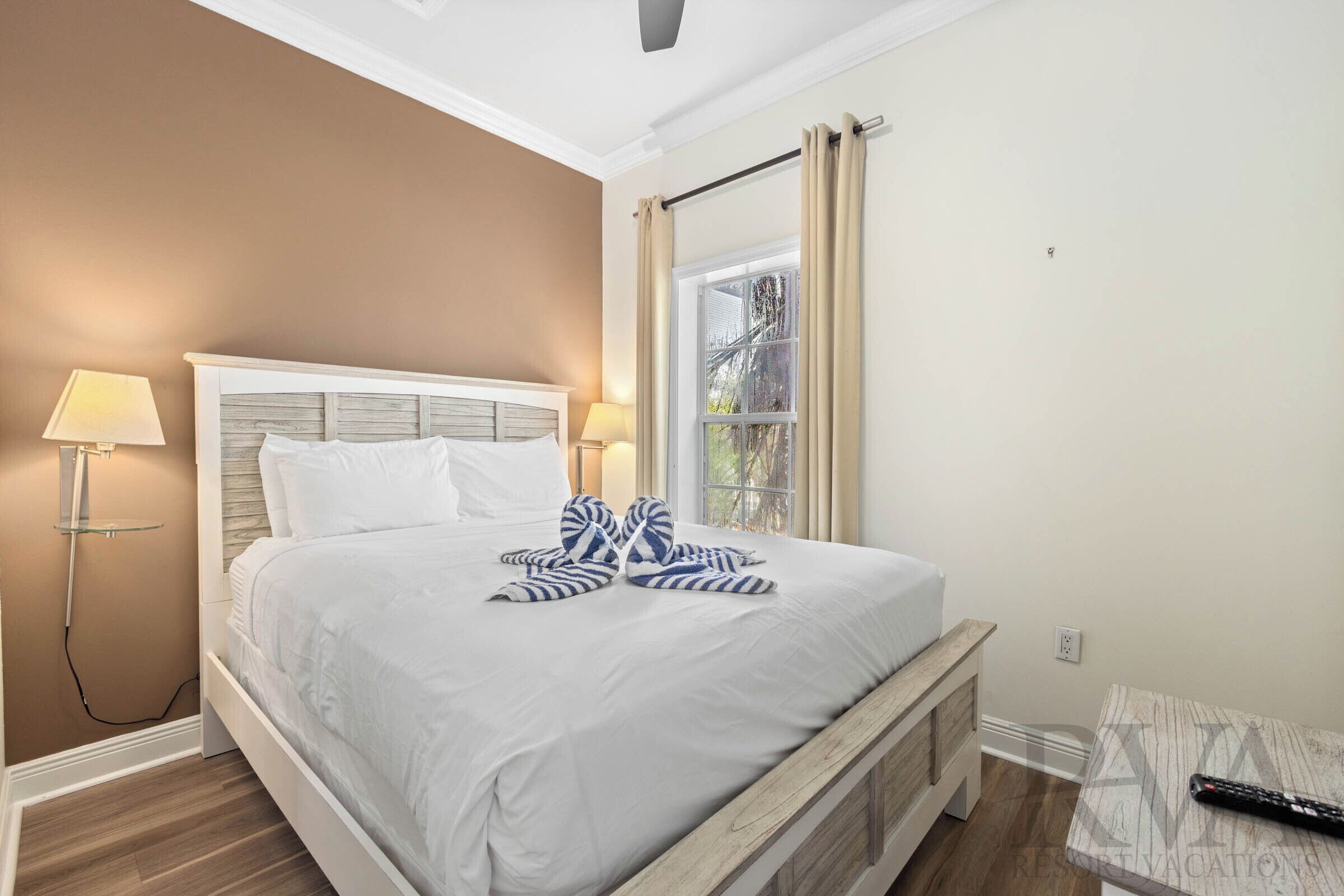 A neatly made bed with white linens, a bedside lamp, and a remote control on a small table beside it.