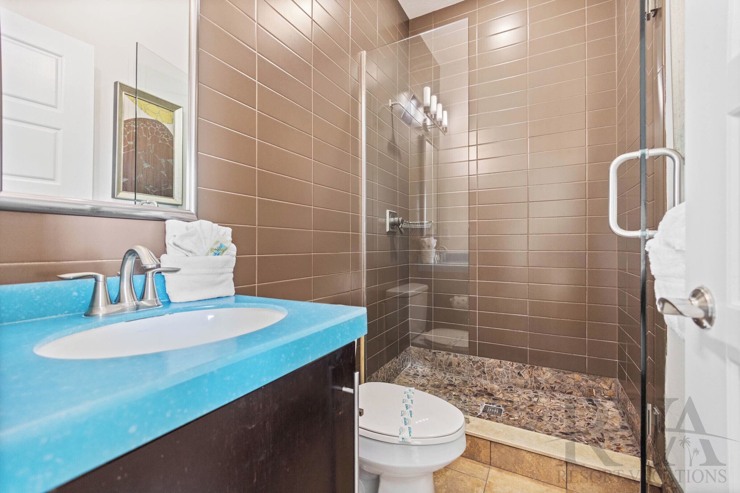 A bathroom with a blue countertop sink, a glass shower enclosure, and a toilet.