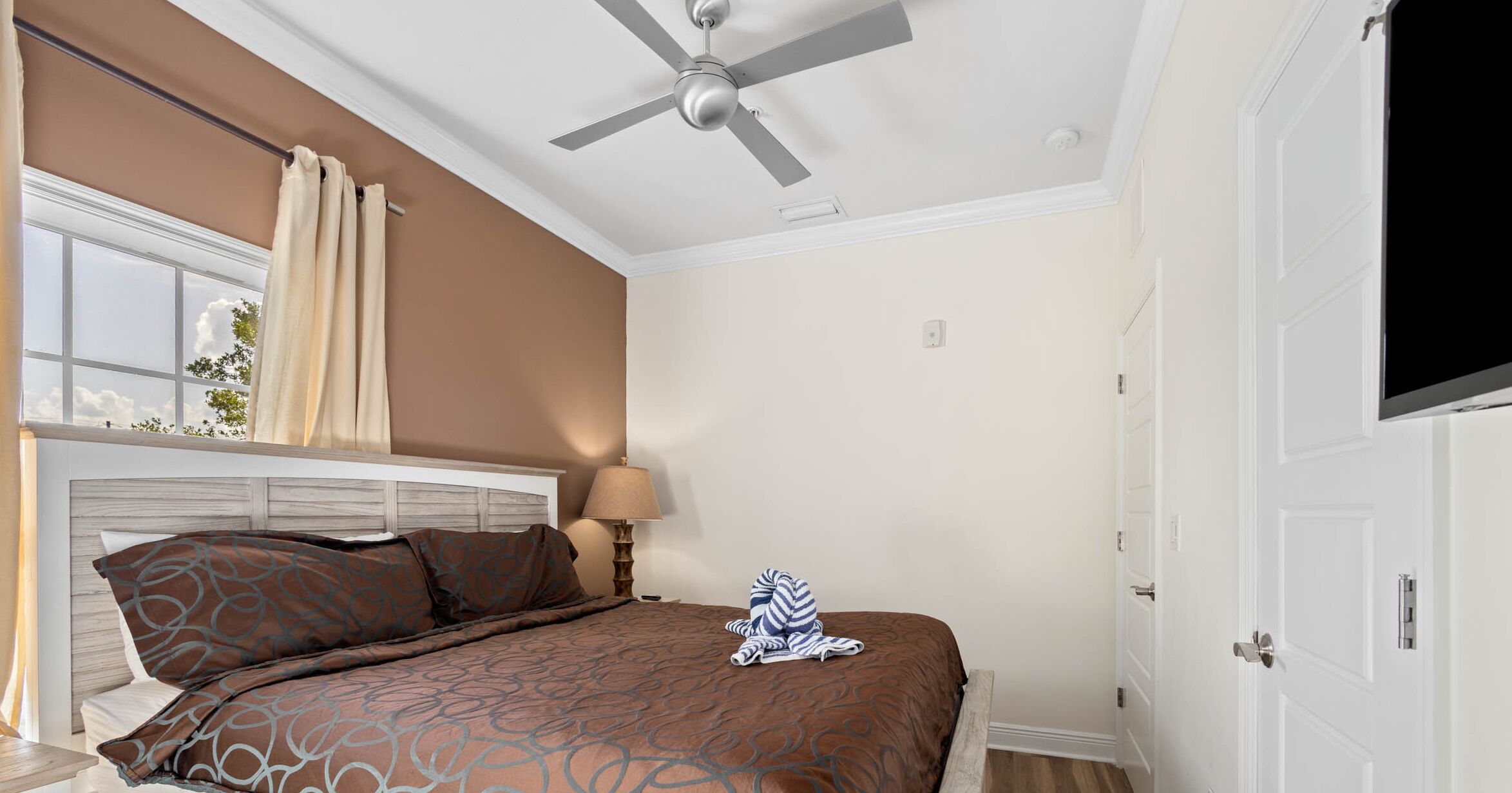 A bedroom with a bed, a ceiling fan, a window with curtains, and a door.