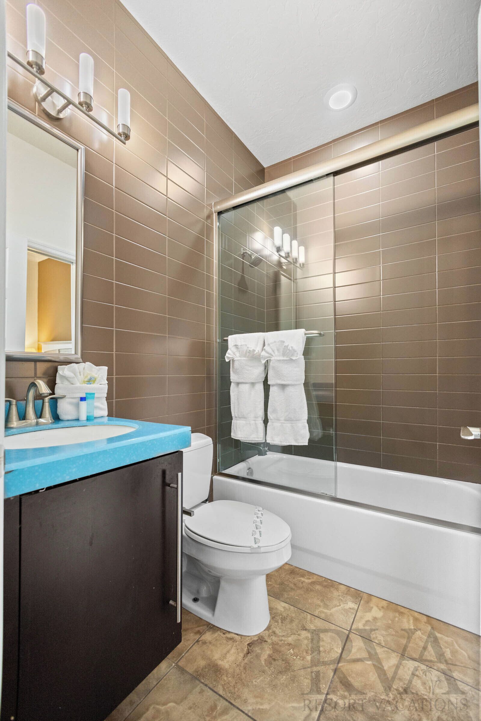 A bathroom with a blue countertop sink, a white toilet, a glass-enclosed shower, and a towel rack with white towels.