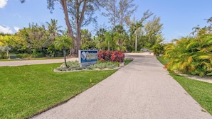 A pathway leading to a sign for Outrigger Resort, surrounded by lush greenery and palm trees. - Ground-Floor Gulf Retreat-Outrigger #5 by RVA (Longboat Key)