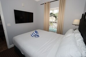 A hotel room with a bed, a TV mounted on the wall, a window with curtains, and a view of an outdoor area. - Relax & Unwind – 1BR Beach Club Siesta Key 110D RVA (Sarasota)