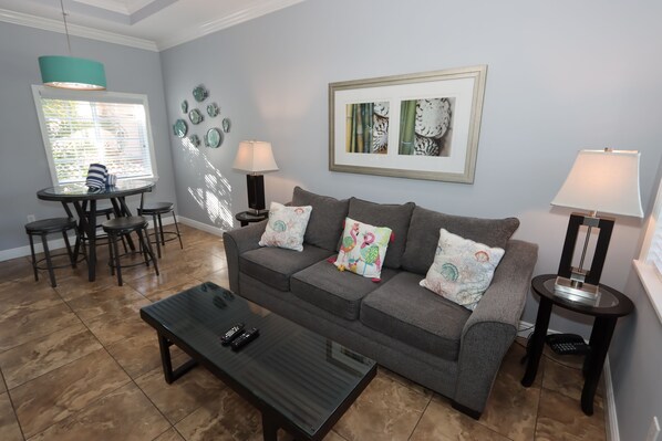 A living room with a grey sofa, a coffee table, a dining table with chairs, and two lamps. - Relax & Unwind – 1BR Beach Club Siesta Key 110D RVA (Sarasota)