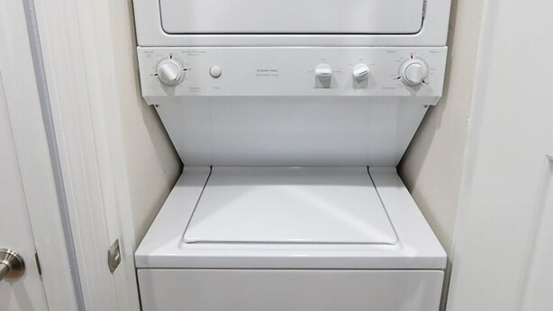 Pequeña lavandería blanca con lavadora y secadora de carga frontal, un panel de control pequeño y una puerta a la izquierda.
