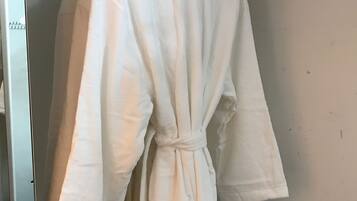 A white robe hanging on a white metal hanger in a room with a white wall and a ceiling with visible pipes.