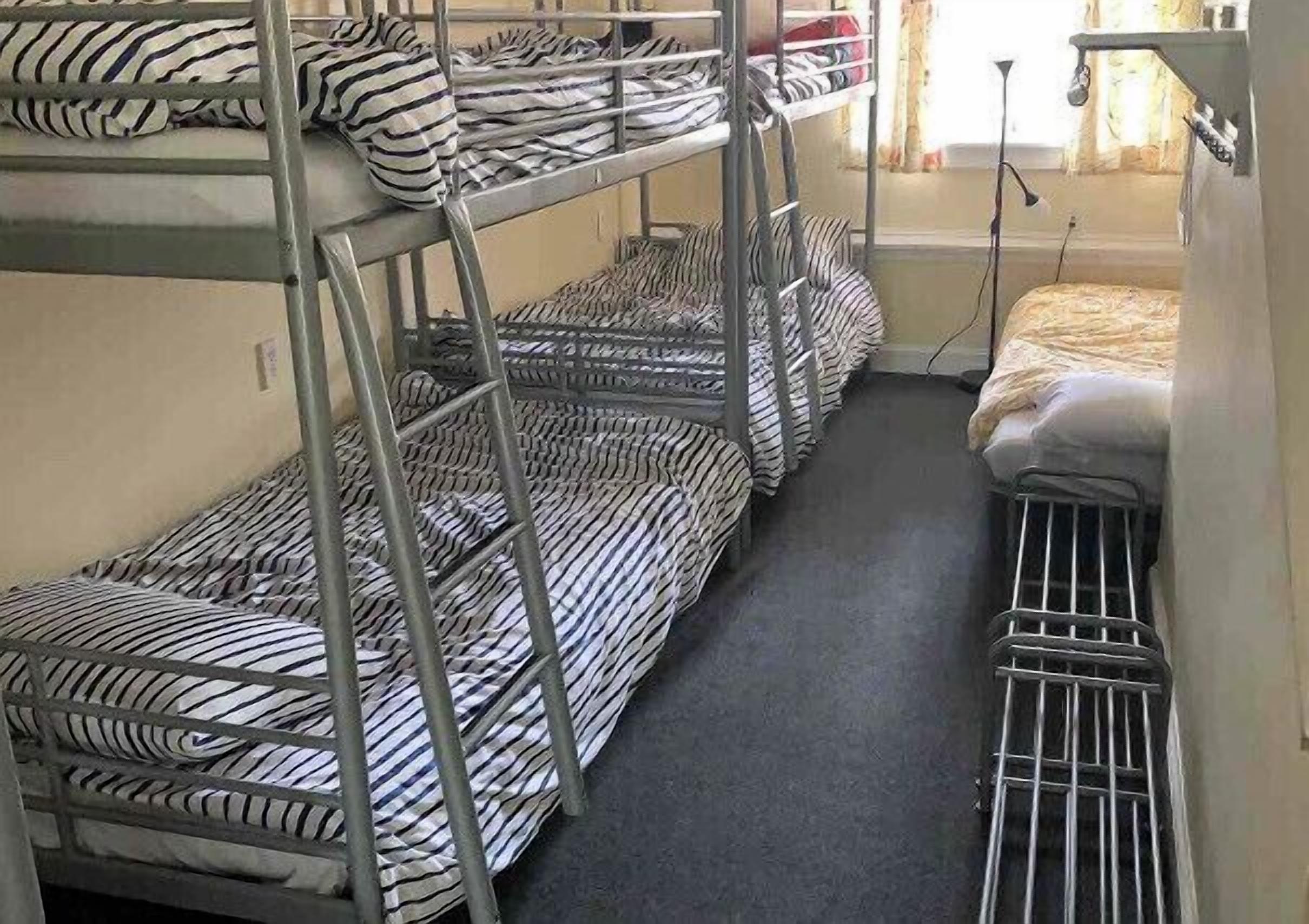 Een slaapkamer met stapelbedden, gestreept beddengoed, een raam met gordijnen en een radiator.