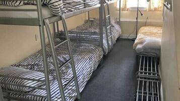 Een slaapkamer met stapelbedden, gestreept beddengoed, een raam met gordijnen en een radiator.