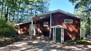 Une cabane avec un porche à l’avant, une porte verte et un petit abri attenant.