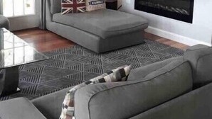 Un salon avec un canapé gris, un téléviseur fixé au mur et une cheminée.