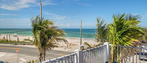 A balcony with a view of the beach, palm trees, and a stop sign.