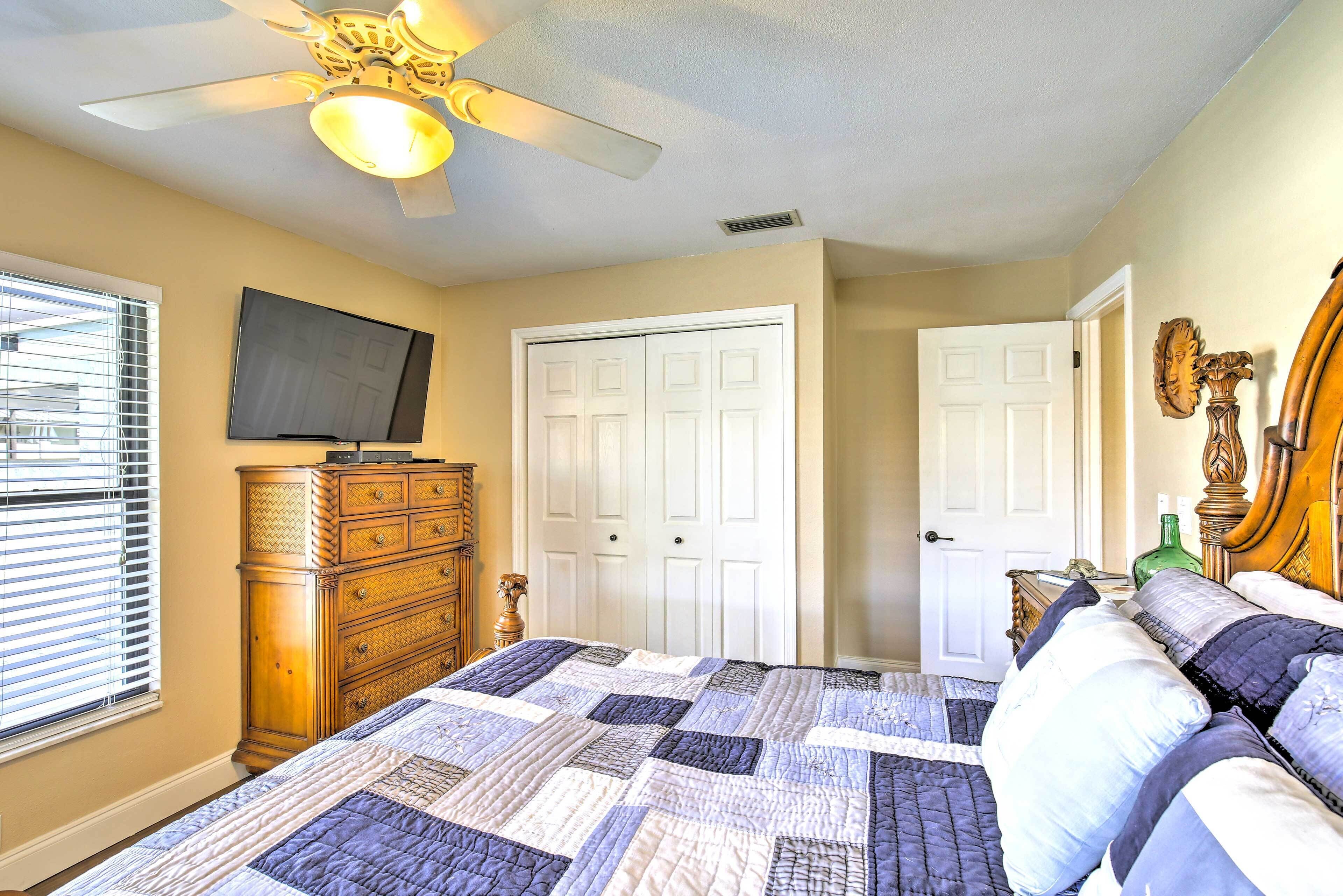 A bedroom with a bed, a ceiling fan, a dresser, a television, and two doors.
