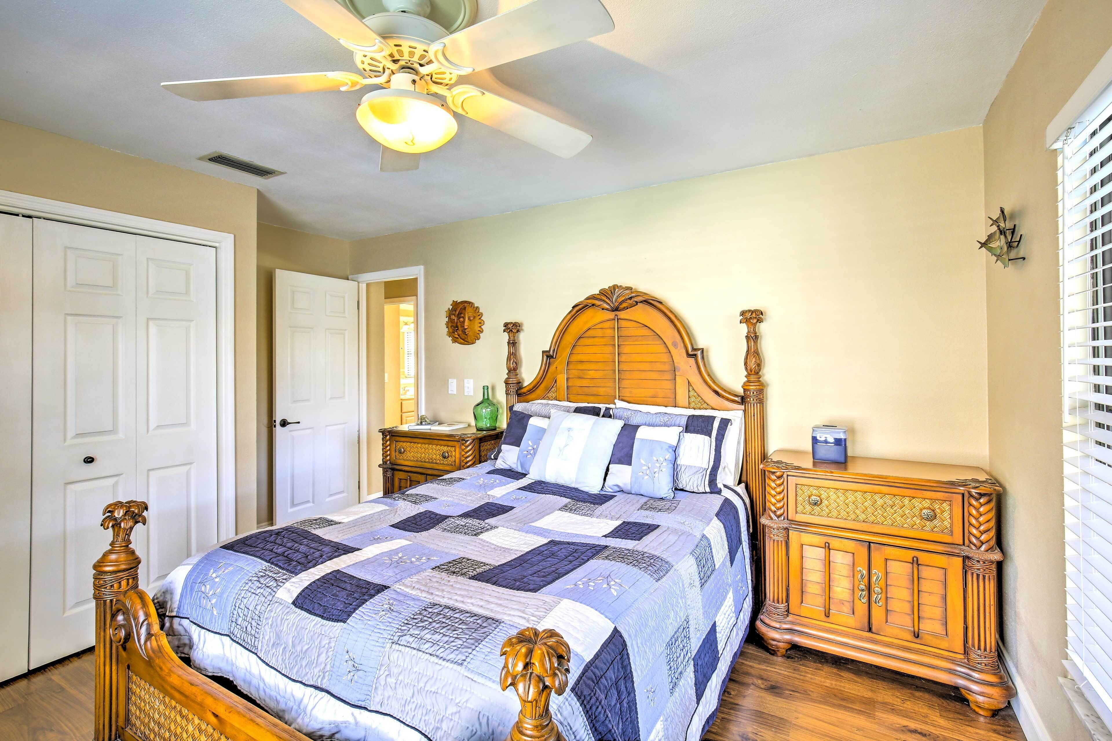 A bedroom with a wooden bed, a nightstand, a dresser, a ceiling fan, and a door.