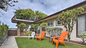Ein Haus mit überdachter Terrasse, zwei orangefarbene Adirondack-Stühle, ein weißer Stuhl und eine kleine Rasenfläche.