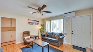 Ein Wohnzimmer mit Deckenventilator, einer Couch, einem Massagesessel, einem Couchtisch und einem großen Fenster mit Jalousien.