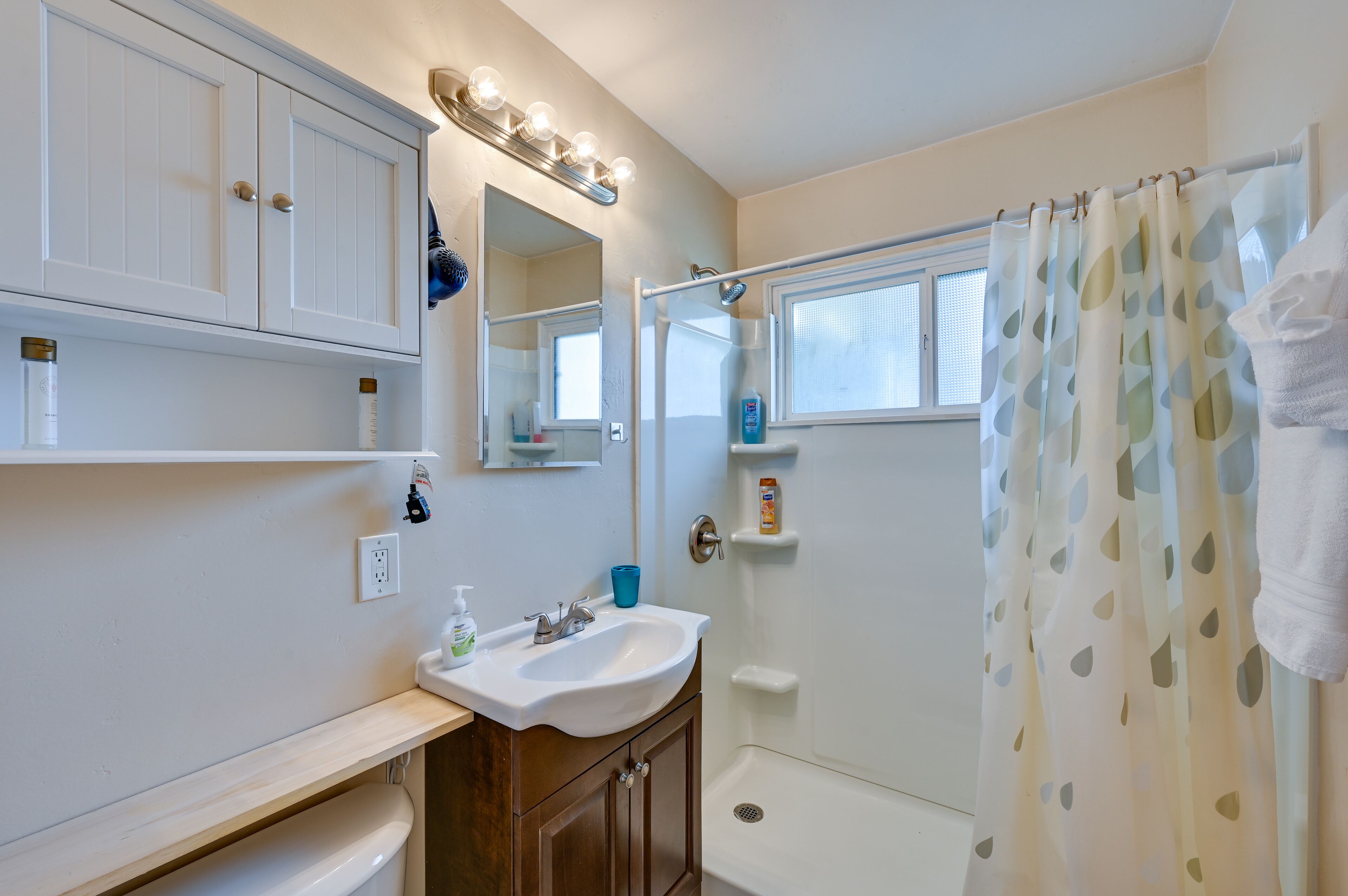 A bathroom with a white sink, vanity, and a shower curtain.