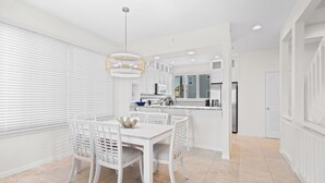 A modern kitchen with white cabinetry, a central island, and a dining area with white chairs and a table. - Play, Stay & Bring Your Pup: Cedars East 832 RVA (Longboat Key)