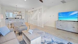 A spacious living area with a large TV, a ceiling fan, and a staircase leading to an upper level. - Play, Stay & Bring Your Pup: Cedars East 832 RVA (Longboat Key)