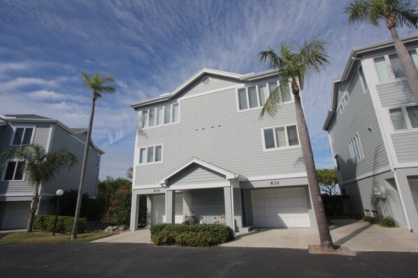 A two-story residential building with a garage, numbered 834, surrounded by palm trees and a clear sky.