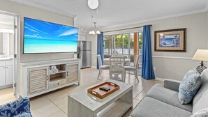 Una sala moderna con televisor de pantalla plana, ventilador de techo y comedor con vista al exterior.
