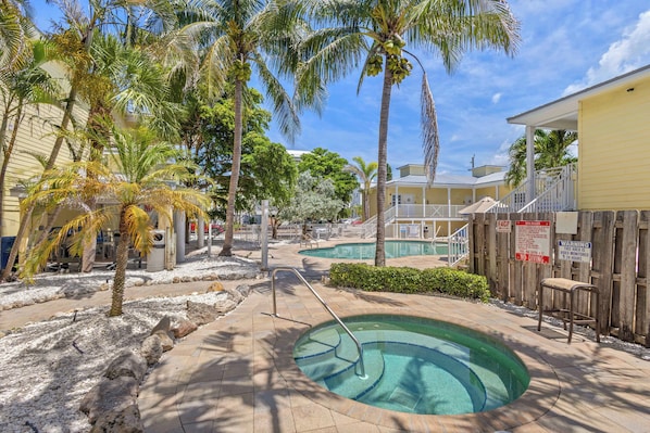 A pool area with palm trees, a small pool, and a wooden fence. - Siesta Key 1-Bedroom Condo | Unit 102B at The Beach Club – Steps to the Beach (Sarasota)