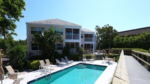 A pool area with lounge chairs and a wooden deck. - Coastal Serenity Sea Twig 102-Beachfront Condo w Private Lanai & Pool by RVA (Longboat Key)