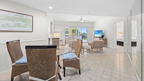 A spacious room with wicker furniture, a glass table, and a television. - Coastal Serenity Sea Twig 102-Beachfront Condo w Private Lanai & Pool by RVA (Longboat Key)