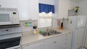 A compact kitchen with white cabinets, a microwave, a stove, a dishwasher, a sink, and a refrigerator. - Siesta Key Getaway – Pet Friendly & Steps to Beach: Siesta Bungalow by RVA (Sarasota)
