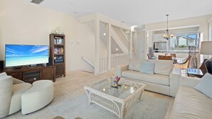 A spacious living room with a large flat-screen TV, a glass coffee table, and a comfortable sofa.