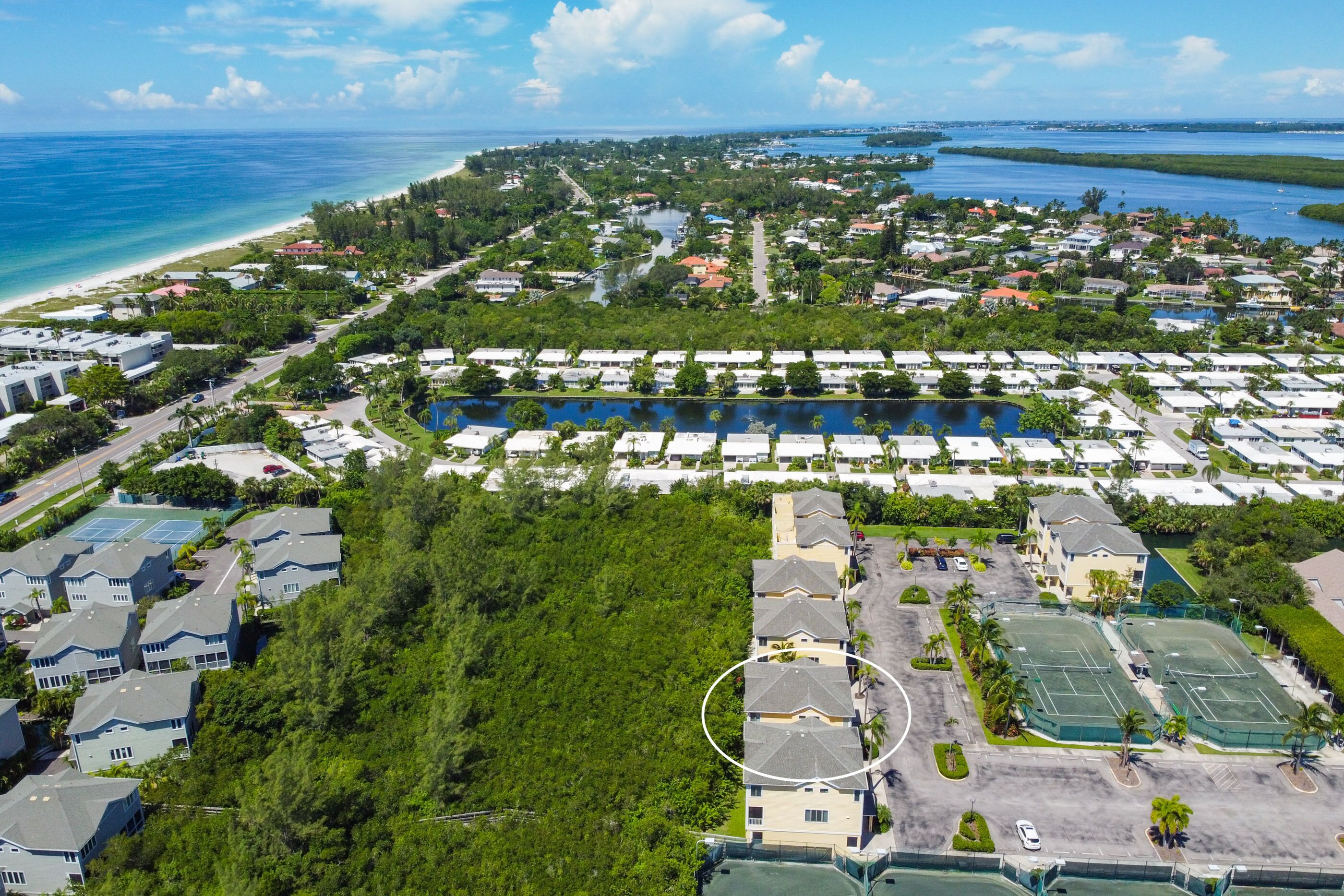 An aerial view of a coastal residential area with a marina, houses, and a large parking lot.
