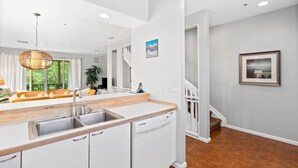 A modern kitchen with white cabinetry, a wooden countertop, and a built-in dishwasher. - Courtside Getaway – Cedars East #605 by RVA (Longboat Key)