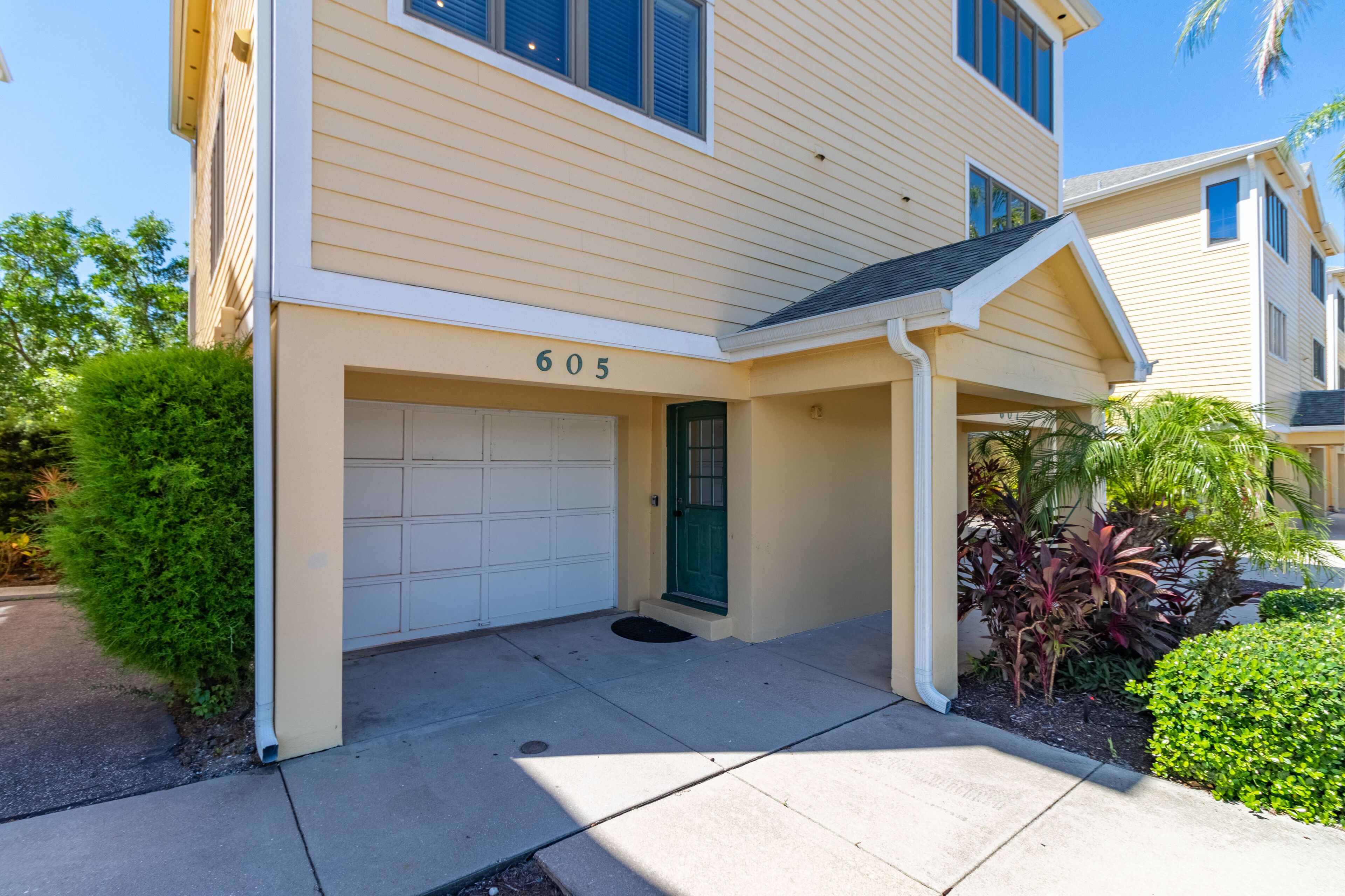 A two-story residential building with a beige exterior, a garage door, and a green door.