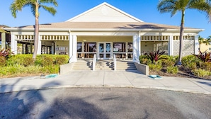 A hotel with a central entrance, palm trees, and a clear blue sky. - Courtside Getaway – Cedars East #605 by RVA (Longboat Key)
