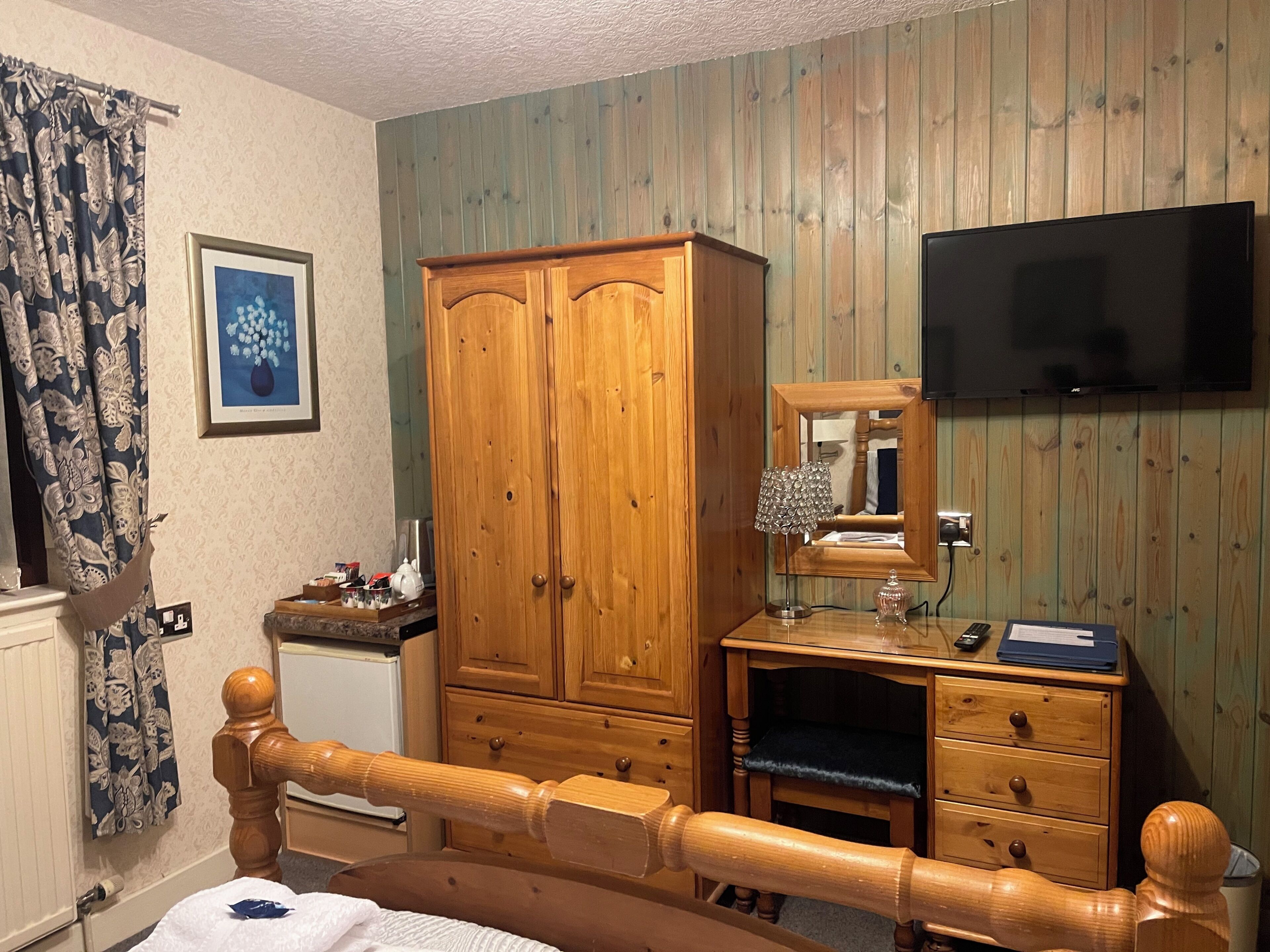A bedroom with a wooden bed, a wardrobe, a dresser, a mirror, a television, and a framed picture on the wall.