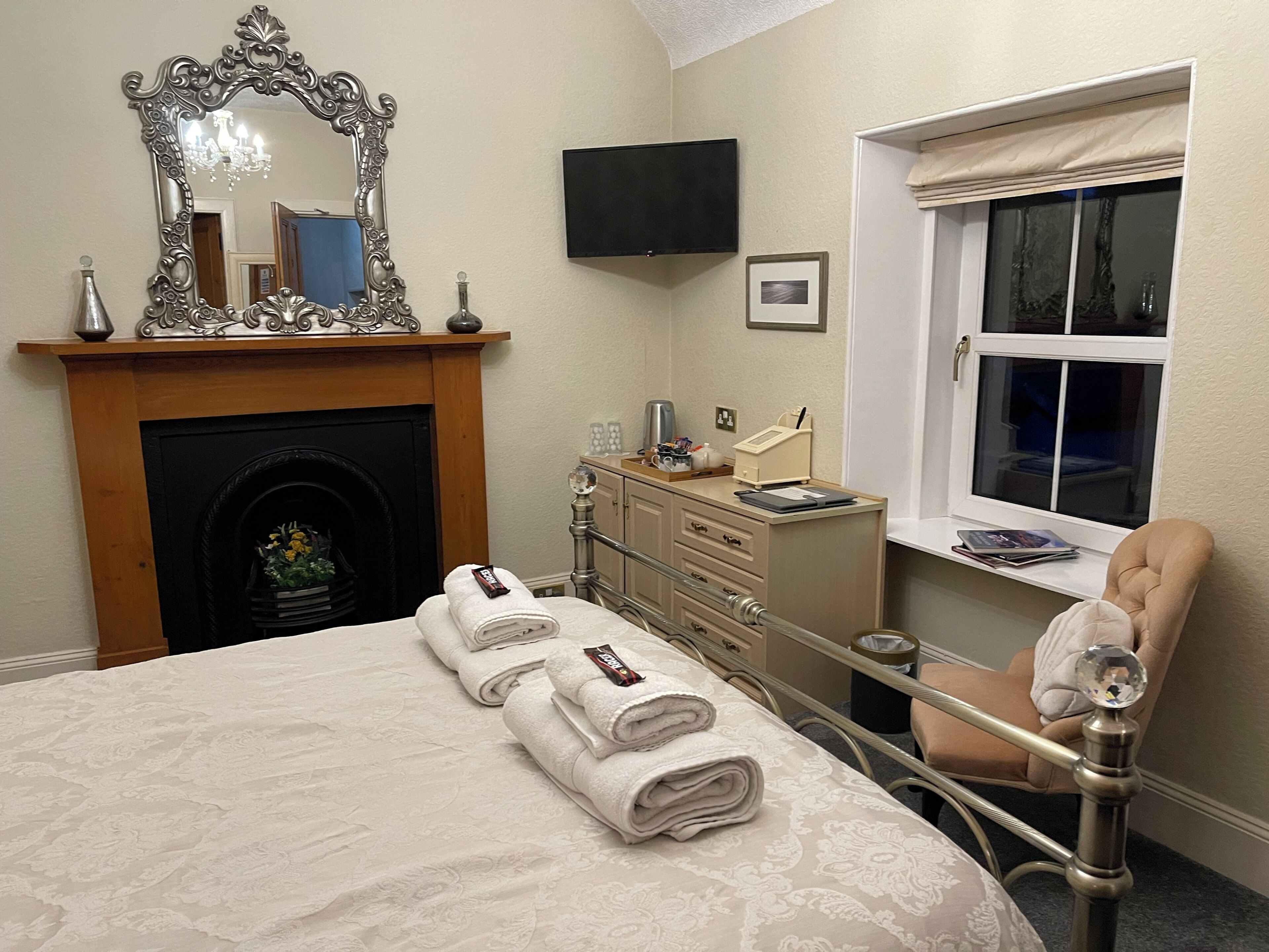 A hotel room with a fireplace, a bed with rolled towels, a dresser, a television, and a window with a view.