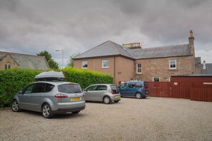 A gravel driveway with parked cars, a stone building with a pitched roof, and a wooden fence. - Dionard Guest House (Inverness)