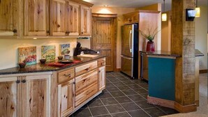 Una cocina con armarios de madera, piso de baldosas negras y un refrigerador.