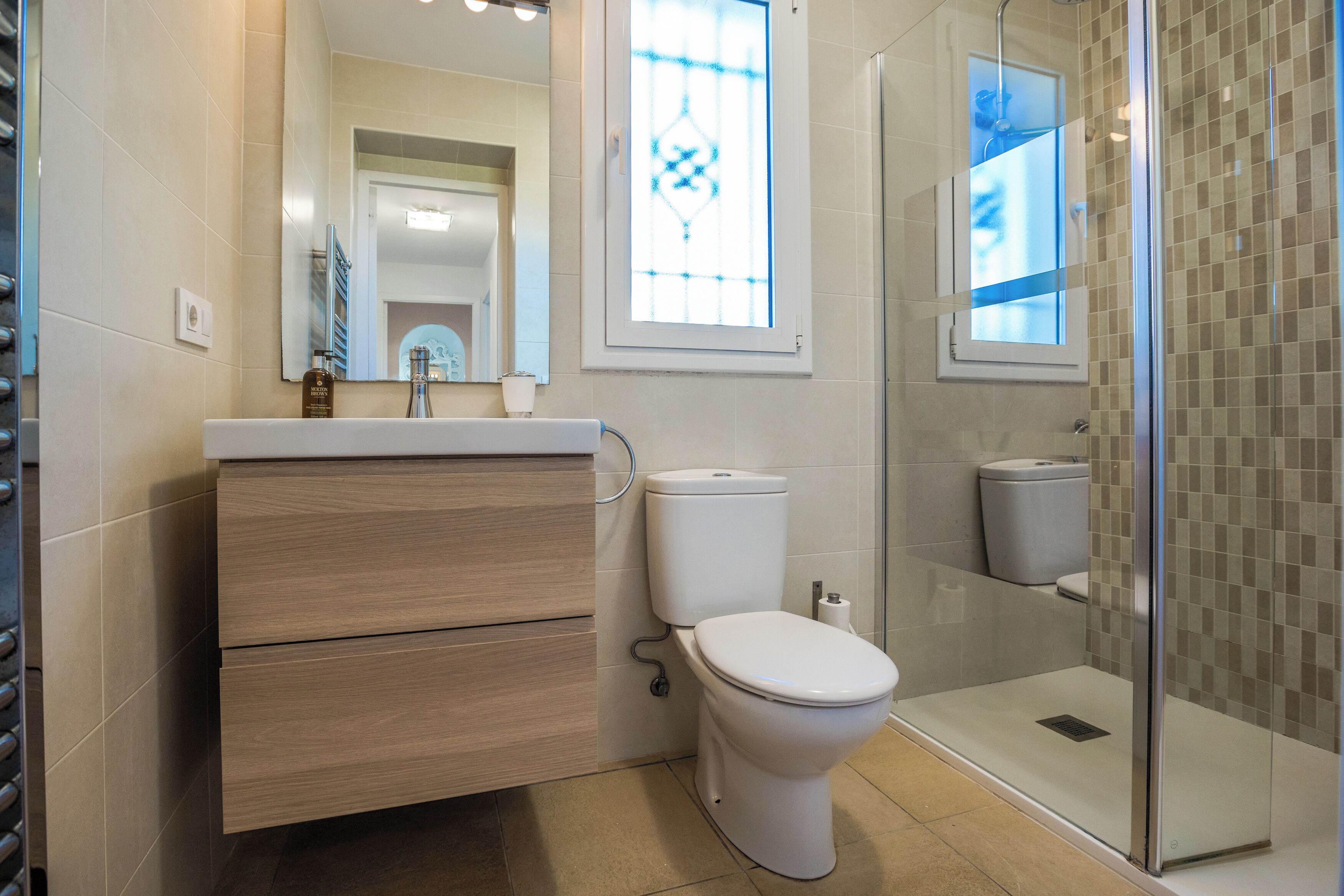 A modern bathroom with a wooden vanity, a toilet, a glass shower enclosure, and a large mirror.