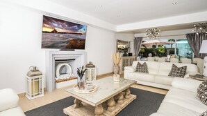 Ein modernes Wohnzimmer mit Kamin, weißen Sofas, einem Couchtisch und einem großen Fernseher, der über dem Kamin angebracht ist.